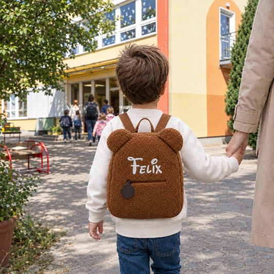 Junge mit braunem Teddy-Rucksack mit dem Namen Felix auf dem Weg in den Kindergarten