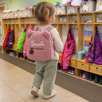 Mädchen mit rosa Teddy-Rucksack mit dem Namen Sophia in der Kita-Garderobe