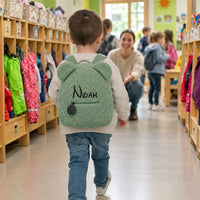 Junge geht mit grünem Teddy-Rucksack mit dem Namen Noah in den Kindergarten