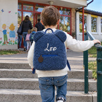 Junge steigt mit blauem Teddy-Rucksack mit dem Namen Leo die Stufen zum Kindergarten hinauf
