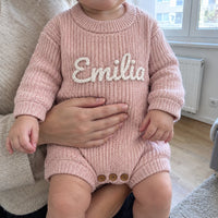 Baby im gestrickten Strampler mit besticktem Namen