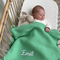Baby im Rattan-Stubenwagen mit gestrickter Babydecke in Mintgrün, Name Emil von Hand im Kettenstich bestickt