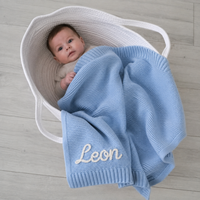 Baby im Stubenkorb mit gestrickter Babydecke in Hellblau, Name Leon von Hand im Kettenstich bestickt