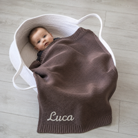 Baby im Stubenkorb mit gestrickter Babydecke in Schokolade, Name Luca von Hand im Kettenstich bestickt