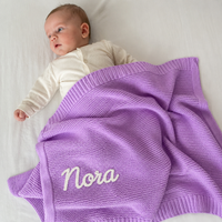 Baby mit gestrickter Babydecke in Flieder, Name Nora von Hand im Kettenstich bestickt