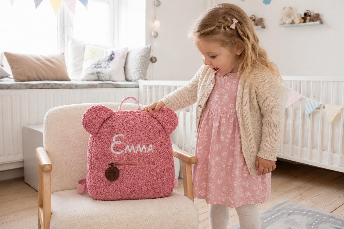 Mädchen entdeckt ihren rosa Teddy Rucksack mit besticktem Namen Emma im Kinderzimmer