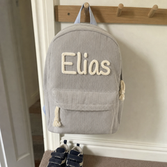 Kundenfoto: grauer Kordsamt-Rucksack mit dem bestickten Namen Elias, an der Garderobe im Flur