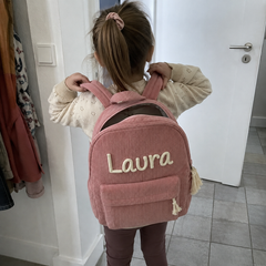 Kundenfoto: Mädchen setzt sich den rosa Kordsamt-Rucksack mit dem bestickten Namen Laura auf