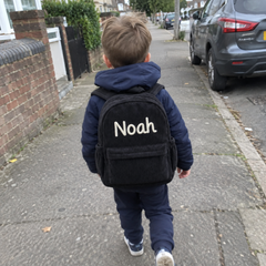 Kundenfoto: Junge trägt den schwarzen Kordsamt-Rucksack mit dem bestickten Namen Noah auf dem Gehweg