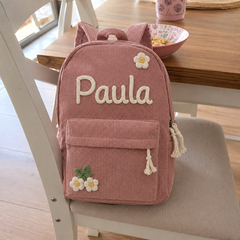 Kundenfoto: rosa Kordsamt-Rucksack mit dem bestickten Namen Paula und Blumen-Applikationen, auf einem Küchenstuhl