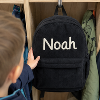 Junge greift nach seinem Kordsamt Rucksack in Schwarz an der Garderobe im Kindergarten, Name Noah in cremefarbener Kettenstich-Stickerei