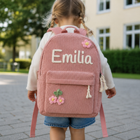 Kleines Mädchen von hinten mit dem Kordsamt Rucksack in Rosa, Name Emilia in cremefarbener Kettenstich-Stickerei, mit gehäkelten Blumen